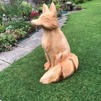 a wooden statue of a fox in a garden