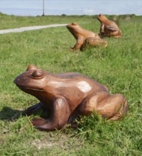 a group of wooden frog sculptures on a grassy field