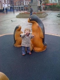 a child standing in front of a group of wooden penguins