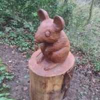 a wooden statue of a mouse sitting on a tree stump
