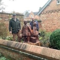 three men standing next to a statue in front of a brick wall