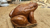a wooden sculpture of a frog sitting on a pallet