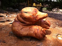 a wooden sculpture of a bear sitting on top of a pile of dirt