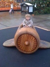 a child sitting in a wooden airplane at an amusement park