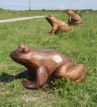 three wooden frog sculptures on a grassy field